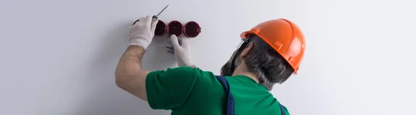 電気技師はアパートにソケットをインストールします オレンジのヘルメットの男と全体は家の中で電気を作る — ストック写真
