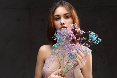 Zarif, çıplak bir beden giymiş güzel seksi bir bayan elinde çiçekler tutuyor. Moda mankeni kızın güzel portresi stüdyoda..