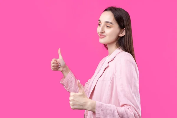 ピンクのジャケットに身を包んだ幸せな若い白人女性が親指を立てて微笑む 良い仕事と尊敬 — ストック写真