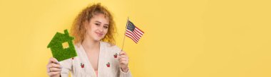 Genç bir kız elinde yeşil bir evin ve bir Amerikan bayrağının modelini tutuyor. Ekonomik ev alma kavramı.