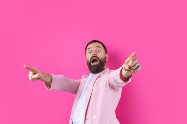 Pembe ceketli bir adam pembe izole edilmiş bir arka planda yön gösterir..