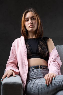 Kız pembe bir ceket ve stüdyoda gri bir kanepede siyah bir bluz giymiş..