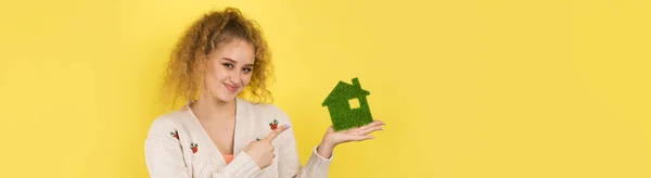 Happy house buyer. A young girl holds a model of a green house in her hands. The concept of green energy, ecology.
