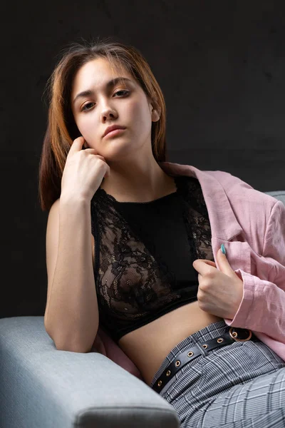 Kız pembe bir ceket ve stüdyoda gri bir kanepede siyah bir bluz giymiş..