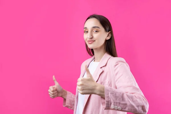 Happy young caucasian female in an pink jacket making thumb up sign and smiling. Good job and respect.