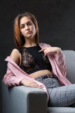 Kız pembe bir ceket ve stüdyoda gri bir kanepede siyah bir bluz giymiş..