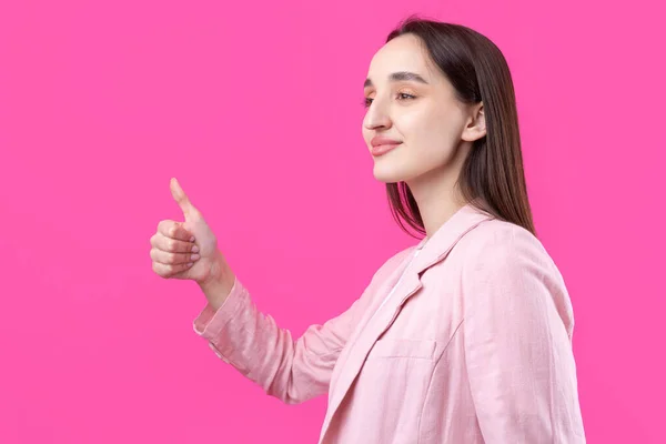 Happy young caucasian female in an pink jacket making thumb up sign and smiling. Good job and respect.