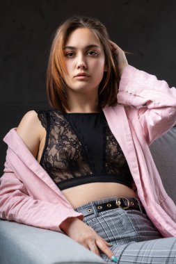 Kız pembe bir ceket ve stüdyoda gri bir kanepede siyah bir bluz giymiş..