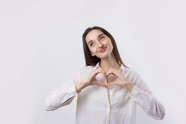 一个微笑的年轻女子的画像 她用手指在白色背景下表现出心脏的动作 免版税图库图片