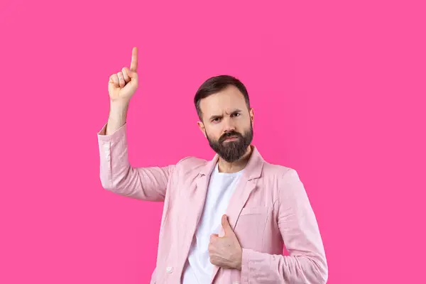 一个穿着粉色夹克的男人在粉红色孤立的背景上指明了方向 图库照片