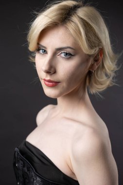 Stüdyoda bir şilin altında etkileyici genç bir sarışın. Siyah bir korse ve elbiseyle.