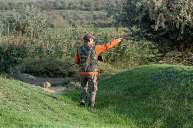 Olgun bir avcı elinde pompalı tüfekle tarlada yürüyor.
