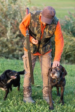 Olgun bir avcı elinde pompalı tüfekle tarlada yürüyor.