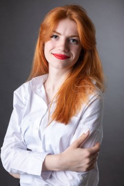 Beyaz gömlekli kızıl saçlı bir kızın portresi. Stüdyoda gri arka planda gülümseyen kadın.