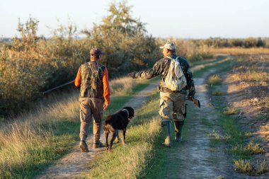 Olgun bir avcı elinde pompalı tüfekle tarlada yürüyor.