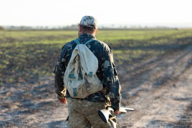 Mature hunter man holding a shotgun and walking through a field clipart