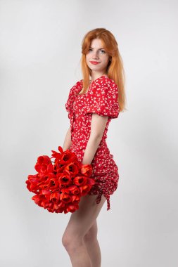 Young happy woman with a bouquet of red lulips. Portrait of a red-haired lady in the studio in front of a white background. clipart