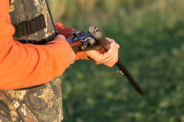 Olgun bir avcı elinde pompalı tüfekle tarlada yürüyor.