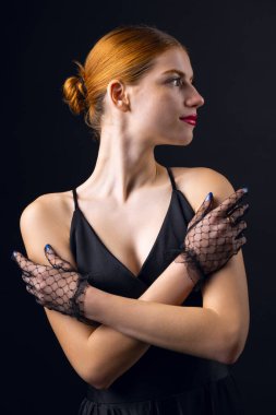 Temiz tenli, siyah eldiven giyen genç bir kızıl kız. Stüdyoda siyah arka planda bir kadının güzel portresi..