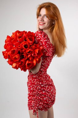 Young happy woman with a bouquet of red lulips. Portrait of a red-haired lady in the studio in front of a white background. clipart