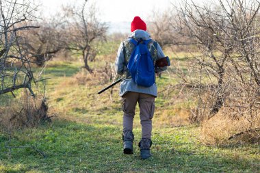 Olgun bir avcı elinde pompalı tüfekle tarlada yürüyor.