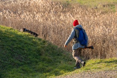 Olgun bir avcı elinde pompalı tüfekle tarlada yürüyor.
