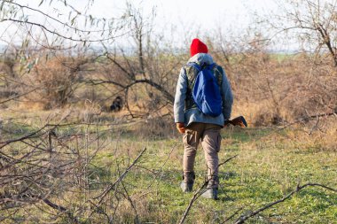 Olgun bir avcı elinde pompalı tüfekle tarlada yürüyor.