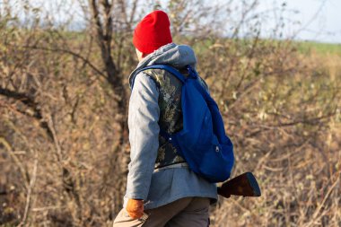 Olgun bir avcı elinde pompalı tüfekle tarlada yürüyor.
