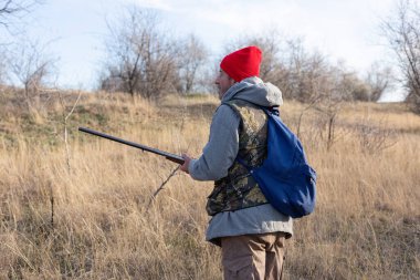 Mature hunter man holding a shotgun and walking through a field clipart