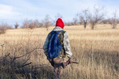 Olgun bir avcı elinde pompalı tüfekle tarlada yürüyor.