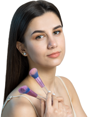 Açık renk bluzlu, beyaz arka planda yüz makyajı yapan genç bir kızın yakın çekimi. Güzel bir kadın yüzüne bir makyaj fırçası tutar ve gülümser..