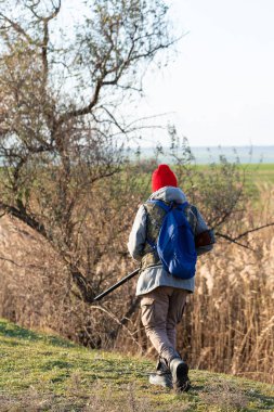 Olgun bir avcı elinde pompalı tüfekle tarlada yürüyor.