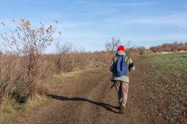 Olgun bir avcı elinde pompalı tüfekle tarlada yürüyor.