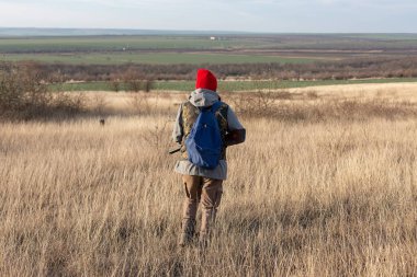 Olgun bir avcı elinde pompalı tüfekle tarlada yürüyor.