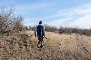 Olgun bir avcı elinde pompalı tüfekle tarlada yürüyor.