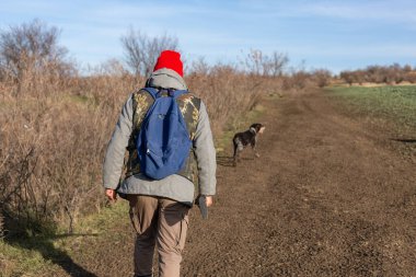 Olgun bir avcı elinde pompalı tüfekle tarlada yürüyor.