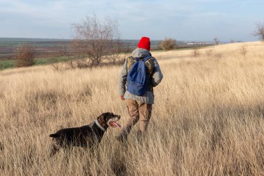 Olgun bir avcı elinde pompalı tüfekle tarlada yürüyor.