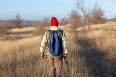 Olgun bir avcı elinde pompalı tüfekle tarlada yürüyor.