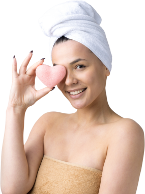 Kafasında beyaz havluyla güzel bir kadın portresi ve pembe bir kalbe bakan bir vücut için sünger. Cilt temizleme eko organik kozmetik rahatlama konsepti.