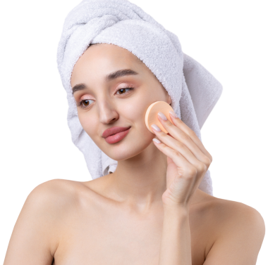 Kalın kaşlı güzel bir kız, beyaz arka planda mükemmel bir ten, kafasında havlu, güzel bir fotoğraf. Kozmetik sünger tutuyor..