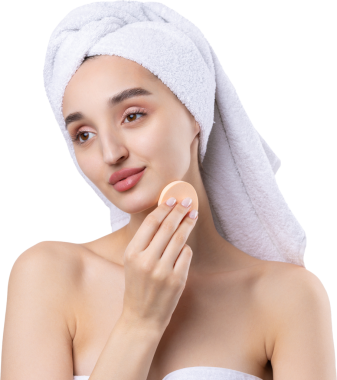 Kalın kaşlı güzel bir kız, beyaz arka planda mükemmel bir ten, kafasında havlu, güzel bir fotoğraf. Kozmetik sünger tutuyor..