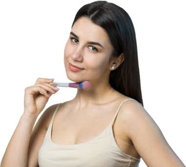 Açık renk bluzlu, beyaz arka planda yüz makyajı yapan genç bir kızın yakın çekimi. Güzel bir kadın yüzüne bir makyaj fırçası tutar ve gülümser..