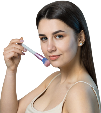 Açık renk bluzlu, beyaz arka planda yüz makyajı yapan genç bir kızın yakın çekimi. Güzel bir kadın yüzüne bir makyaj fırçası tutar ve gülümser..