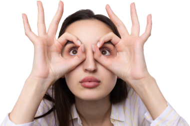 Beyaz stüdyo arka planında güzel bir jest sergileyen ve elleriyle dürbün yapan çekici genç kadının portresini kapat..