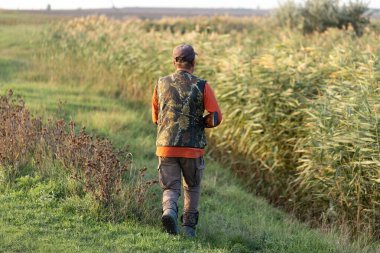 Olgun bir avcı elinde pompalı tüfekle tarlada yürüyor.