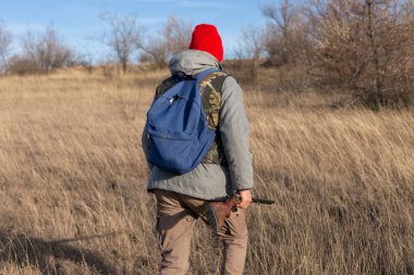 Olgun bir avcı elinde pompalı tüfekle tarlada yürüyor.