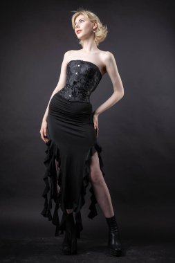 Stüdyoda bir şilin altında etkileyici genç bir sarışın. Siyah bir korse ve elbiseyle.