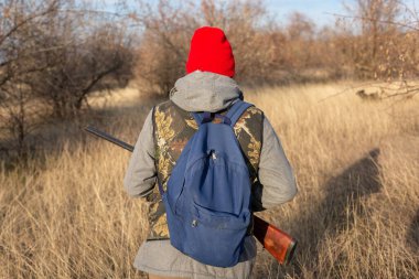 Olgun bir avcı elinde pompalı tüfekle tarlada yürüyor.