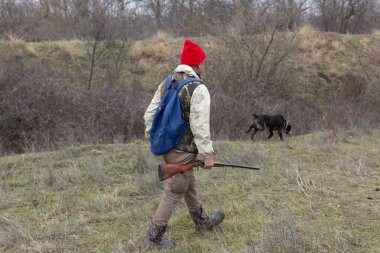 Olgun bir avcı elinde pompalı tüfekle tarlada yürüyor.