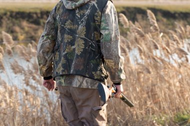 Olgun bir avcı elinde pompalı tüfekle tarlada yürüyor.